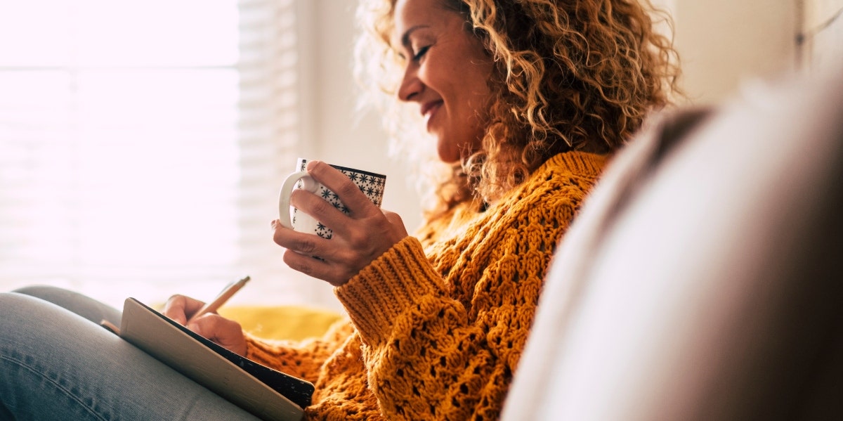 woman writing while holding cup 