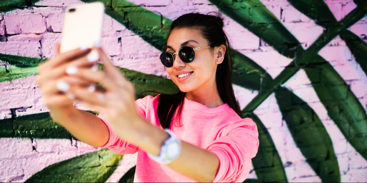 How To Take A Good Selfie By Changing Two Settings On Your iPhone woman taking a selfie with her phone