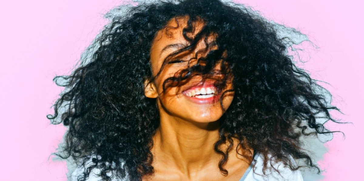 pink background woman smiling with hair in her face