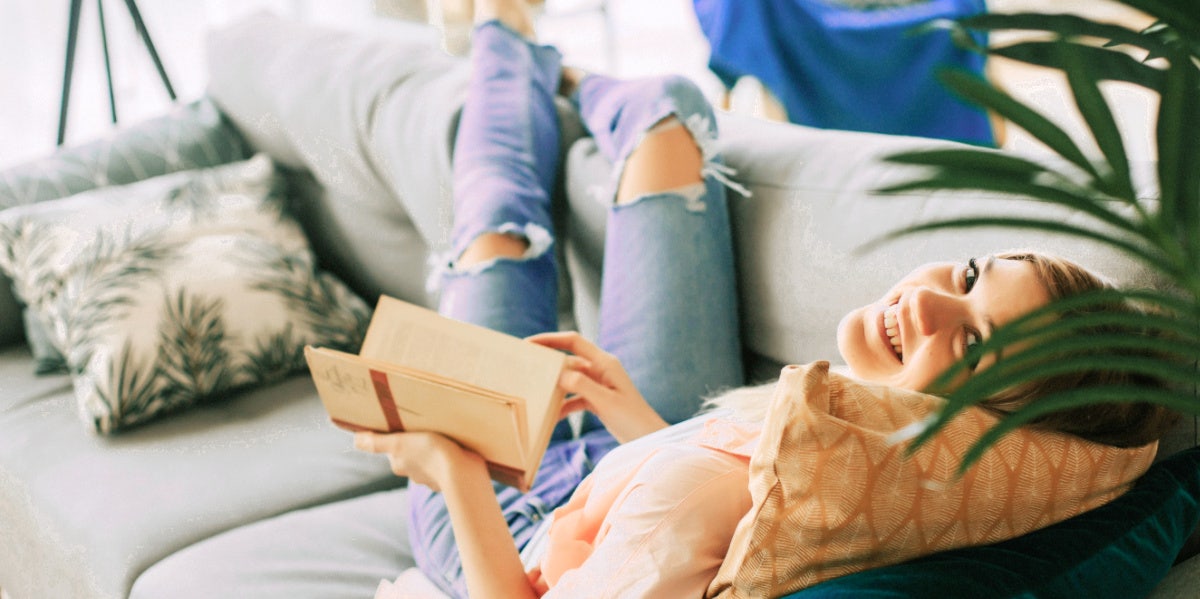 white woman lounges on couch with book trying to transform life