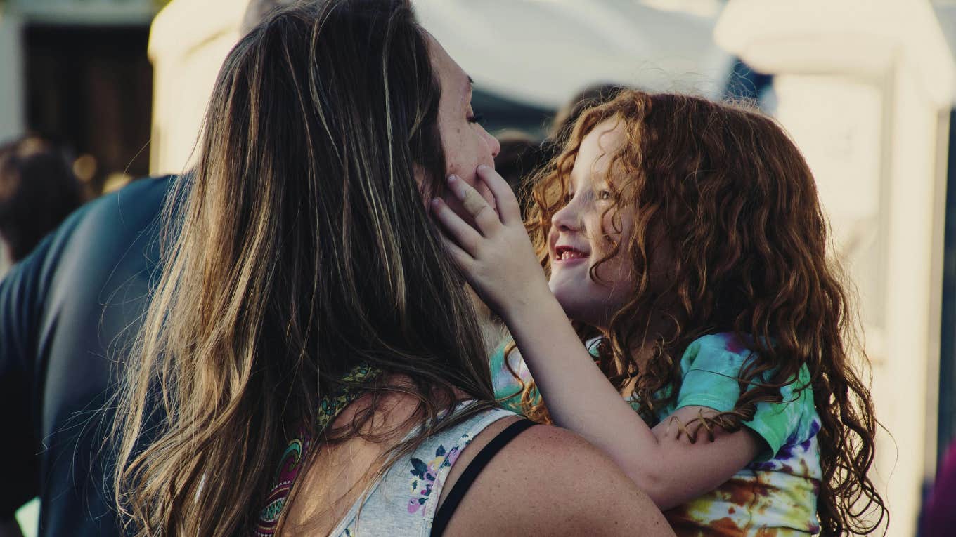 woman carrying little girl who is touching her face