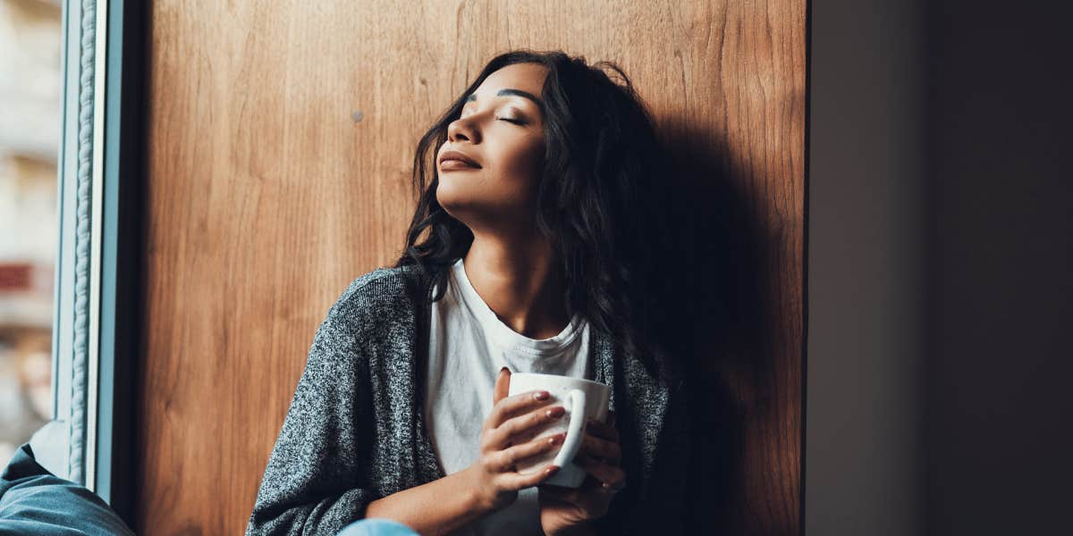 peaceful young woman holding a mug and relaxing by window