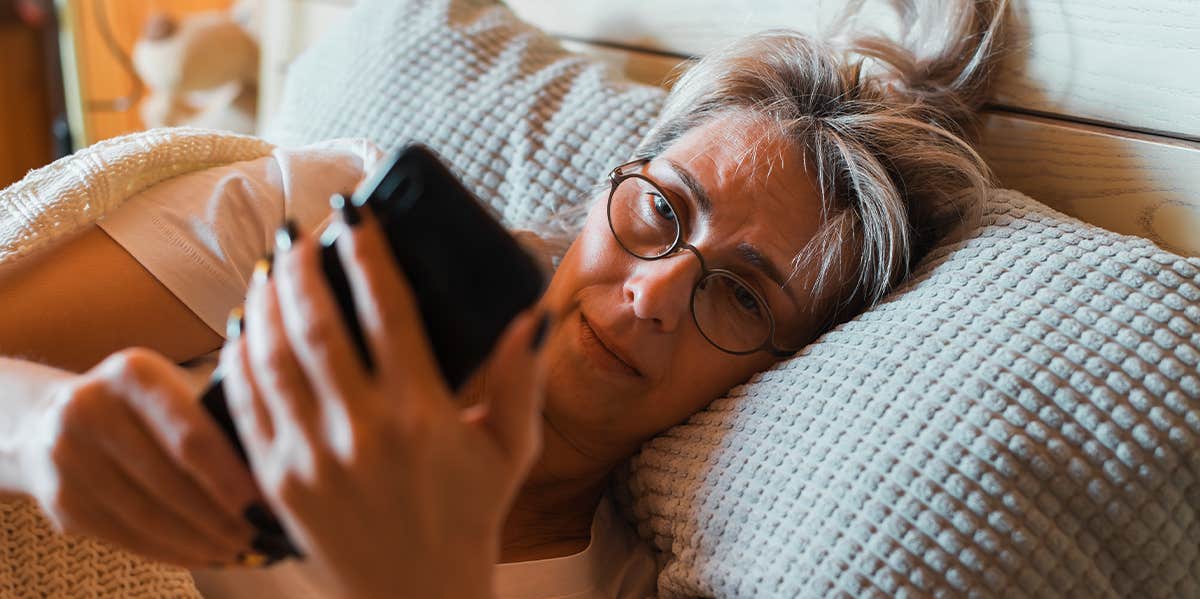 old woman looking at phone in bed