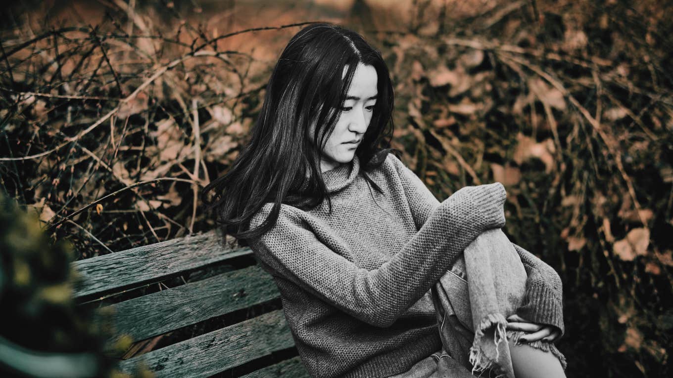 Woman feeling sad, sitting on a bench outside 