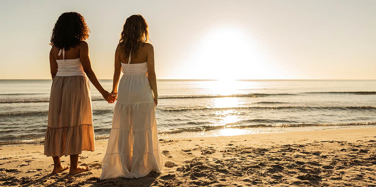 two woman holding hands on the beach