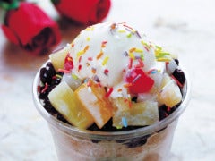 bowl of ice cream with a lot of toppings on table with roses