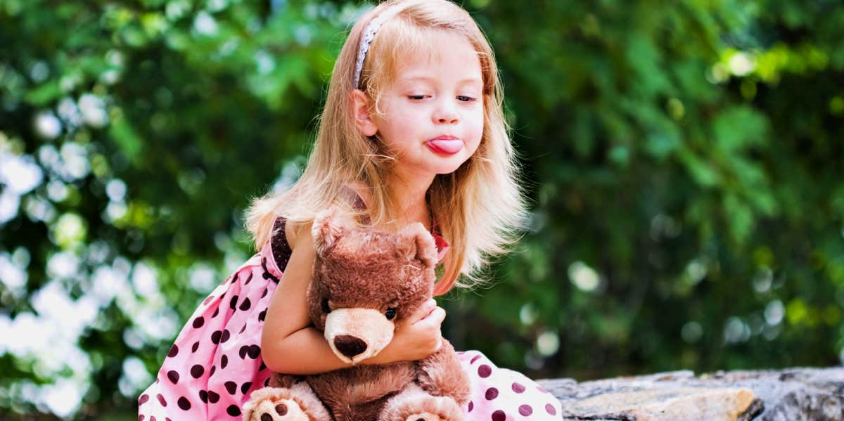 little girl holding teddy bear sticking her tongue out
