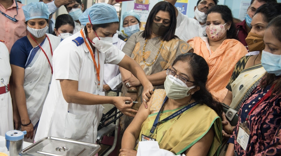 woman getting a vaccine in india while a crowd watches