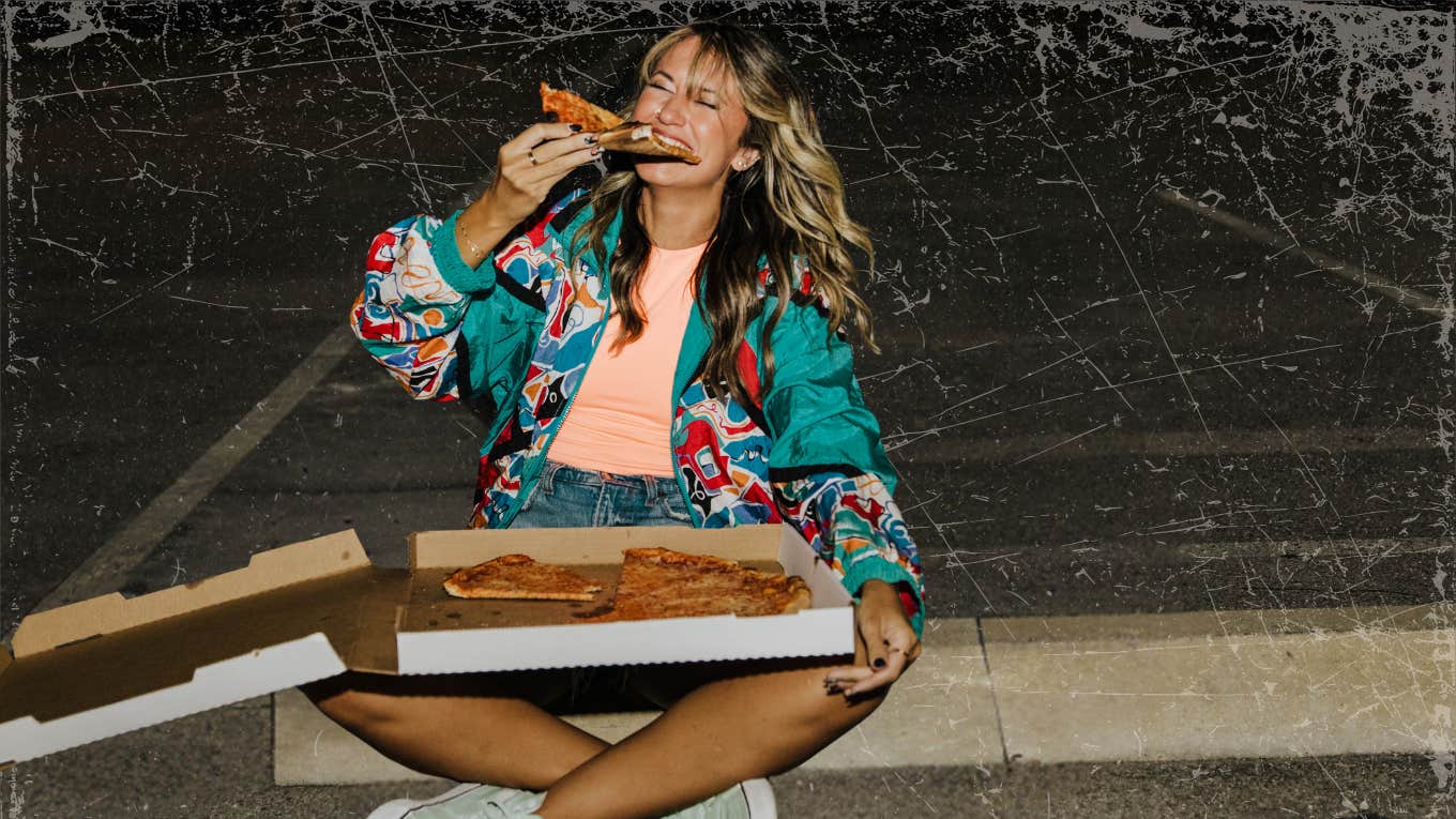 Woman eating pizza on a curb