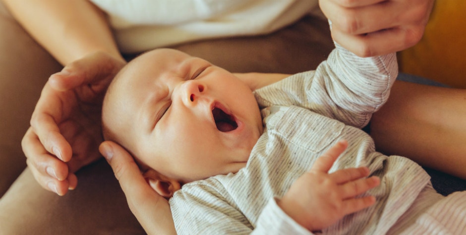 young caucasian baby yawning, held by parents