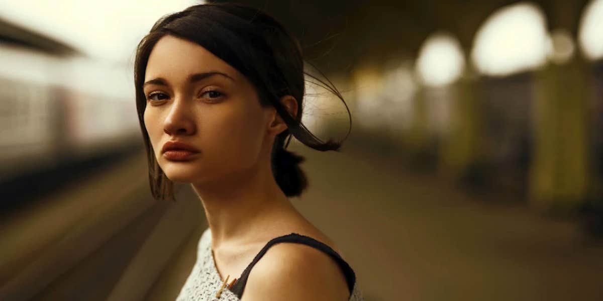 A sad woman looks to the camera with a empty train platform stretching behind her