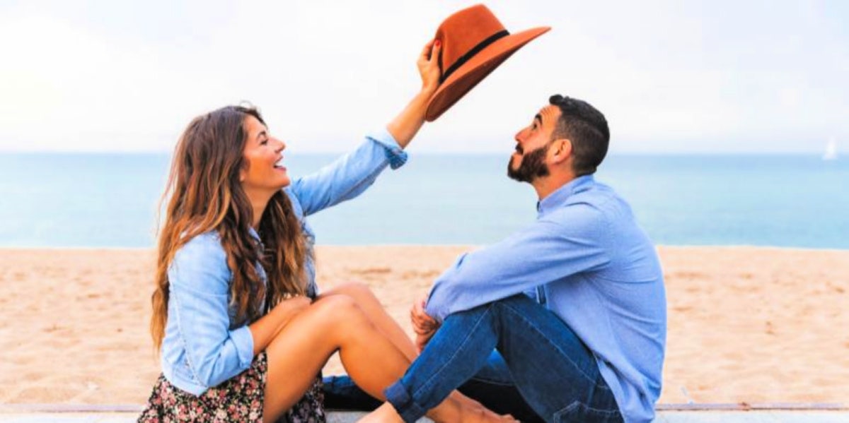 Is He The One? 18 Signs He's The One For You guy and girl smiling on the beach with a hat
