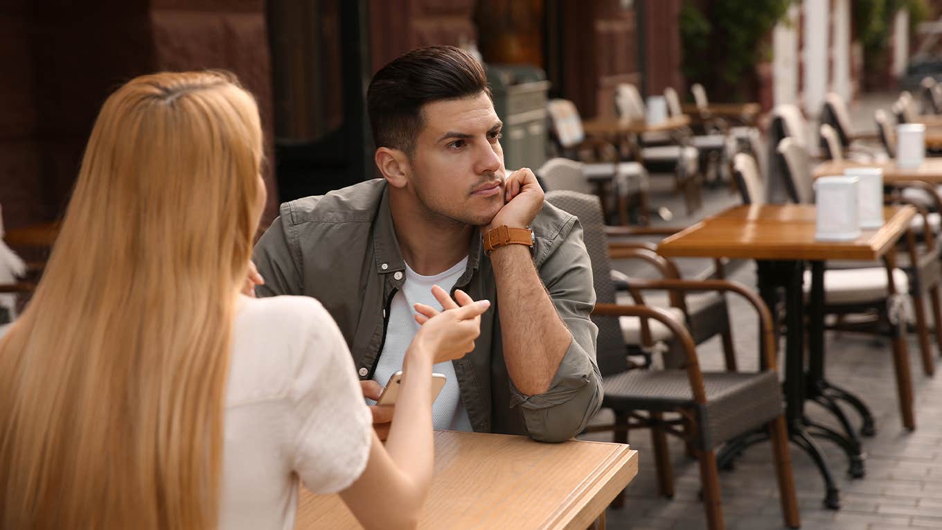 Man getting bored during first date with overtalkative young woman at outdoor cafe