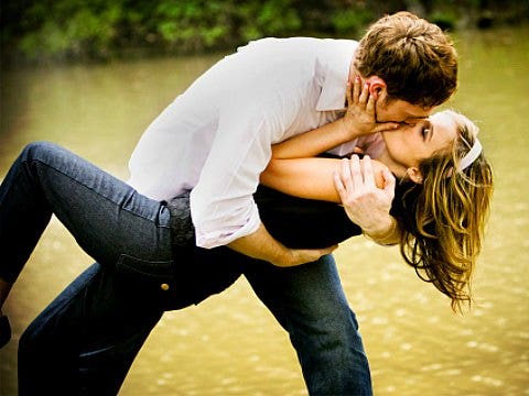 man dipping woman into a kiss by water