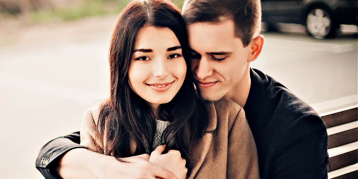 man and woman on a park bench, man hugging her from behind