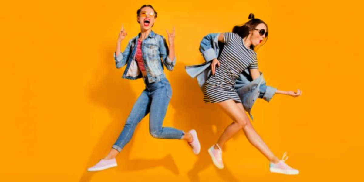 two girls happy jumping yellow background