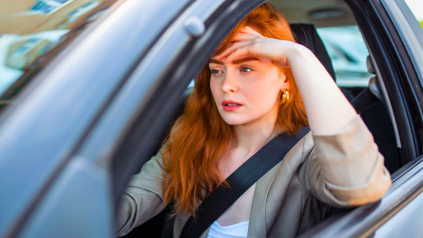 frustrated woman sitting in her car with her hand on her forehead