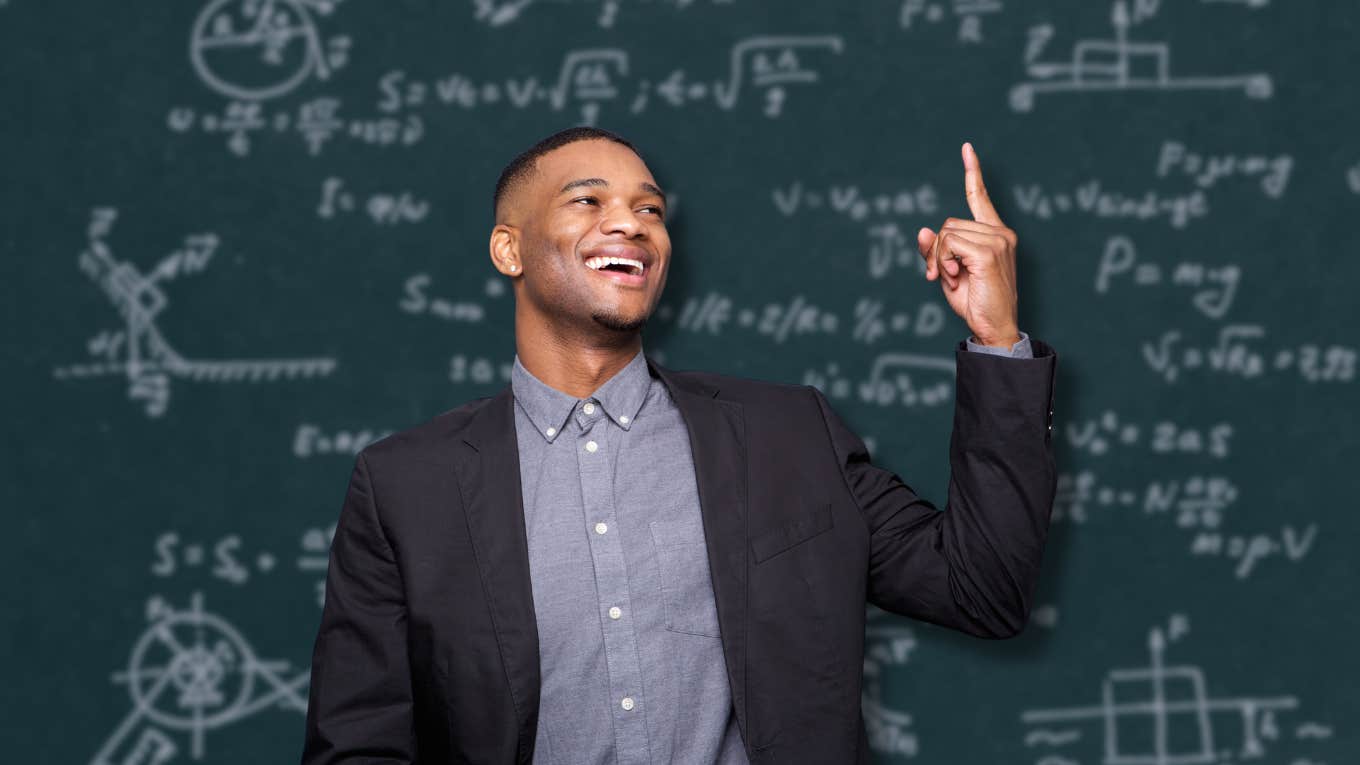 happy man in front of chalkboard with physics problems on it