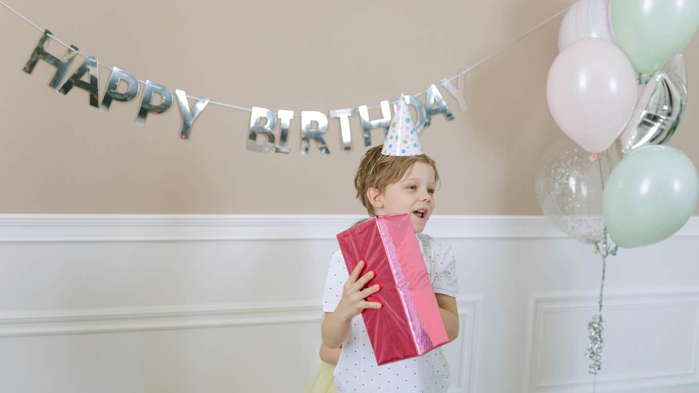 Little Boy Who Asked His Single Dad For A Barbie Party Is Delighted To See His Dad Dressed As Ken At His All-Pink Birthday Celebration boy celebrating his birthday holding a present