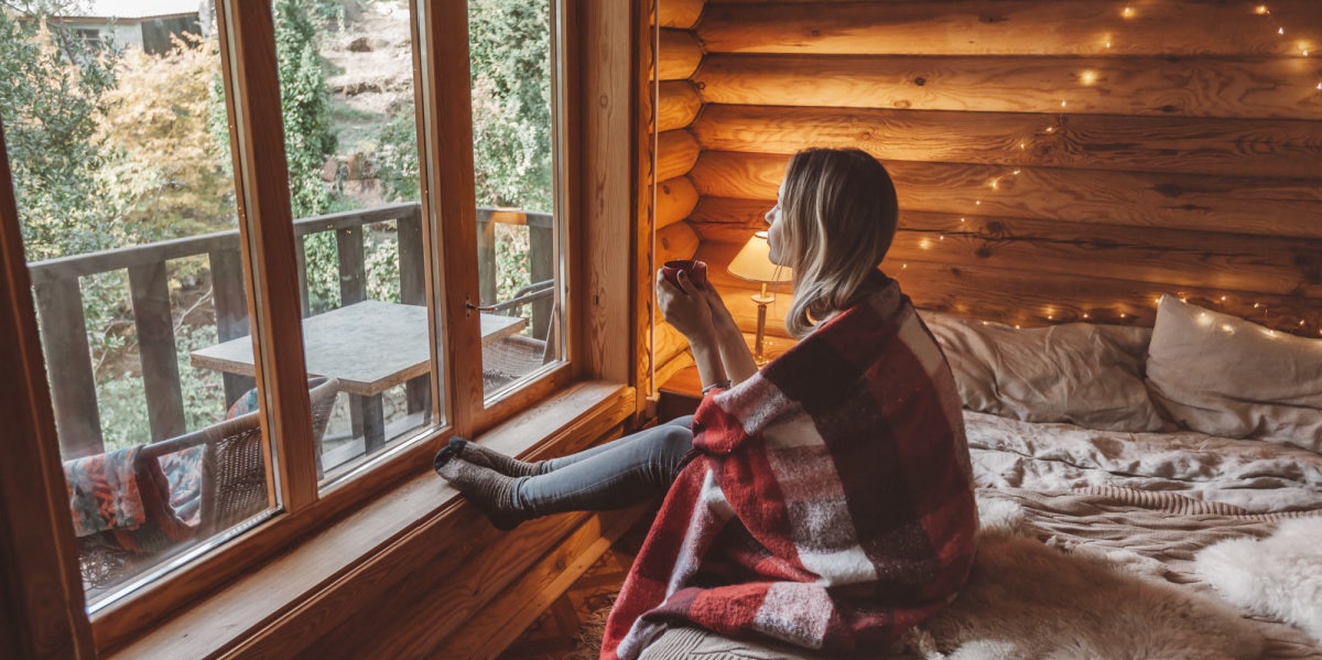 woman with coffee blanket cabin looking out window