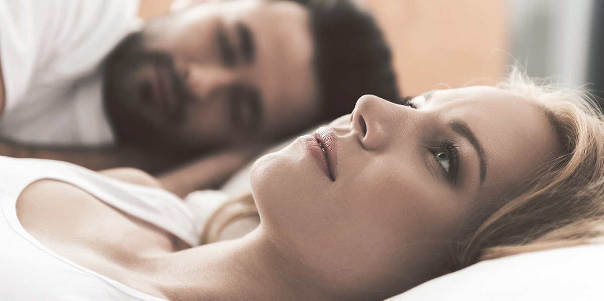 woman looking miserable in bed next to husband 