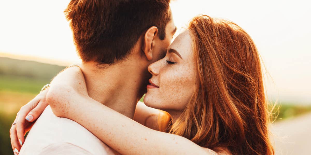 brown haired man looks away while red-haired woman hugs him 