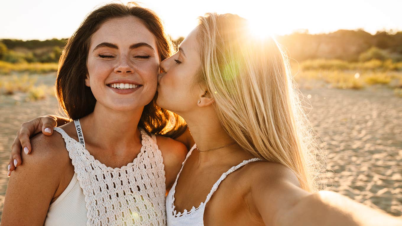 Two young happy women smiling and taking selfie photo while walking on beach