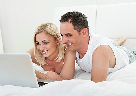 man and woman looking at laptop in bed