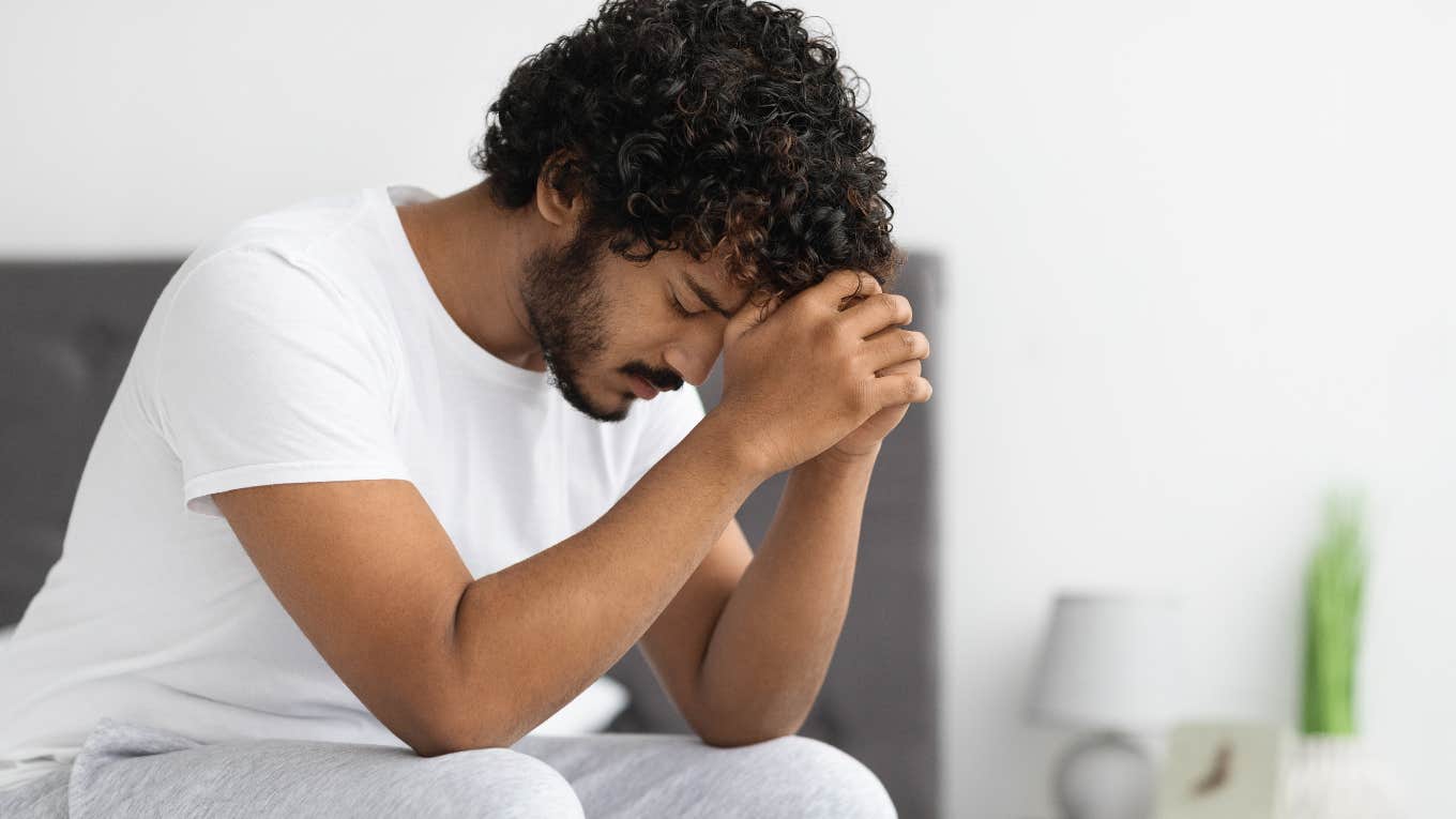 young man in pajamas sitting on bed at home thinking about something