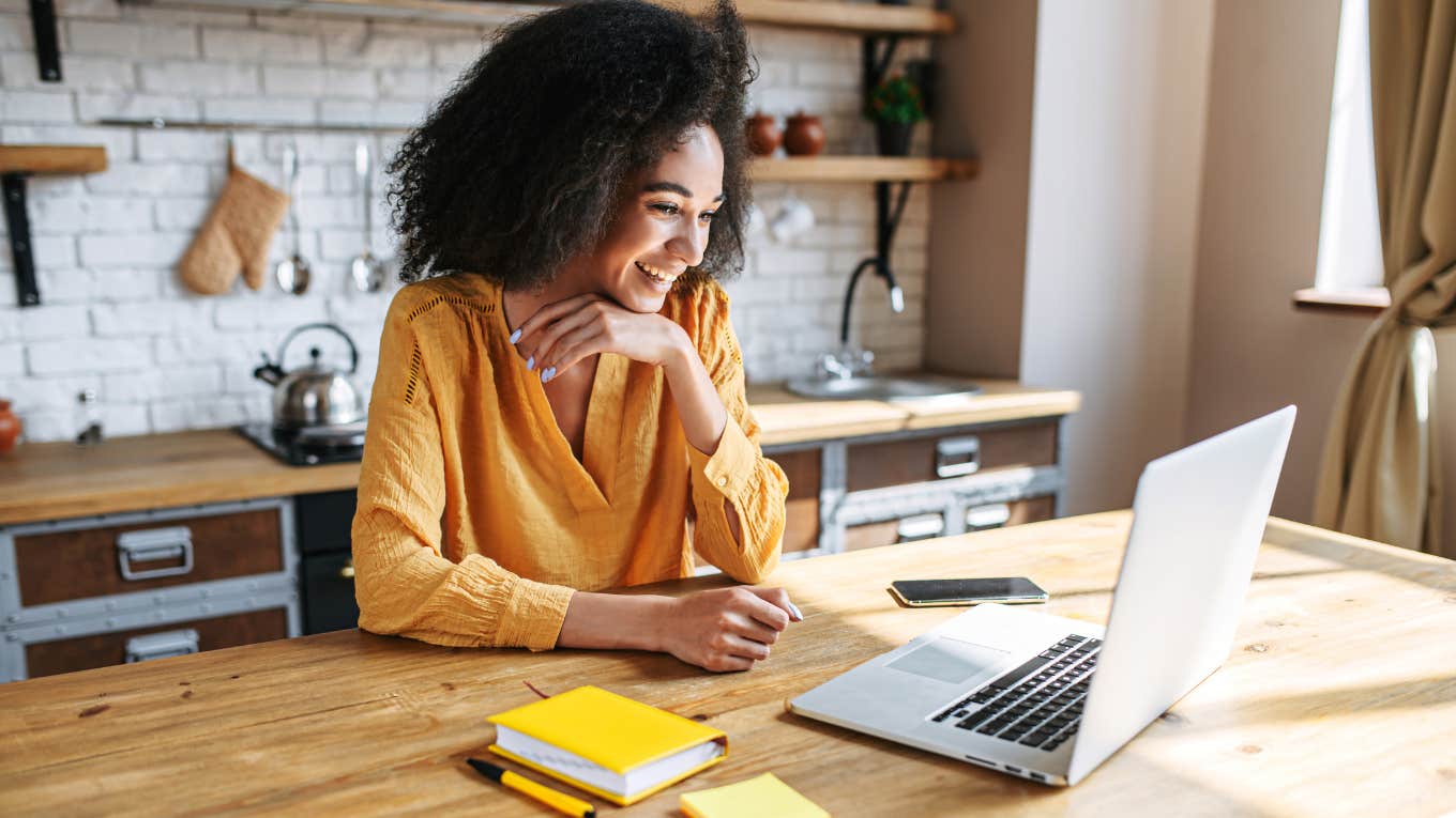 woman uses laptop for remote work while sitting in the kitchen at home.