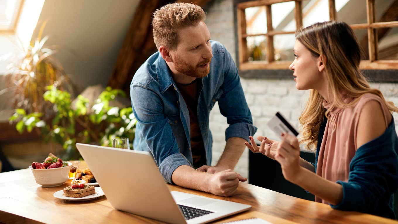 Displeased couple arguing about debt on their credit card while e-banking over laptop at home.