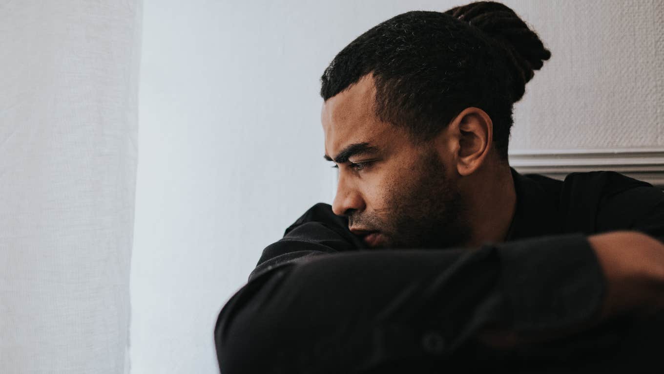 upset man sitting on the floor and looking out window