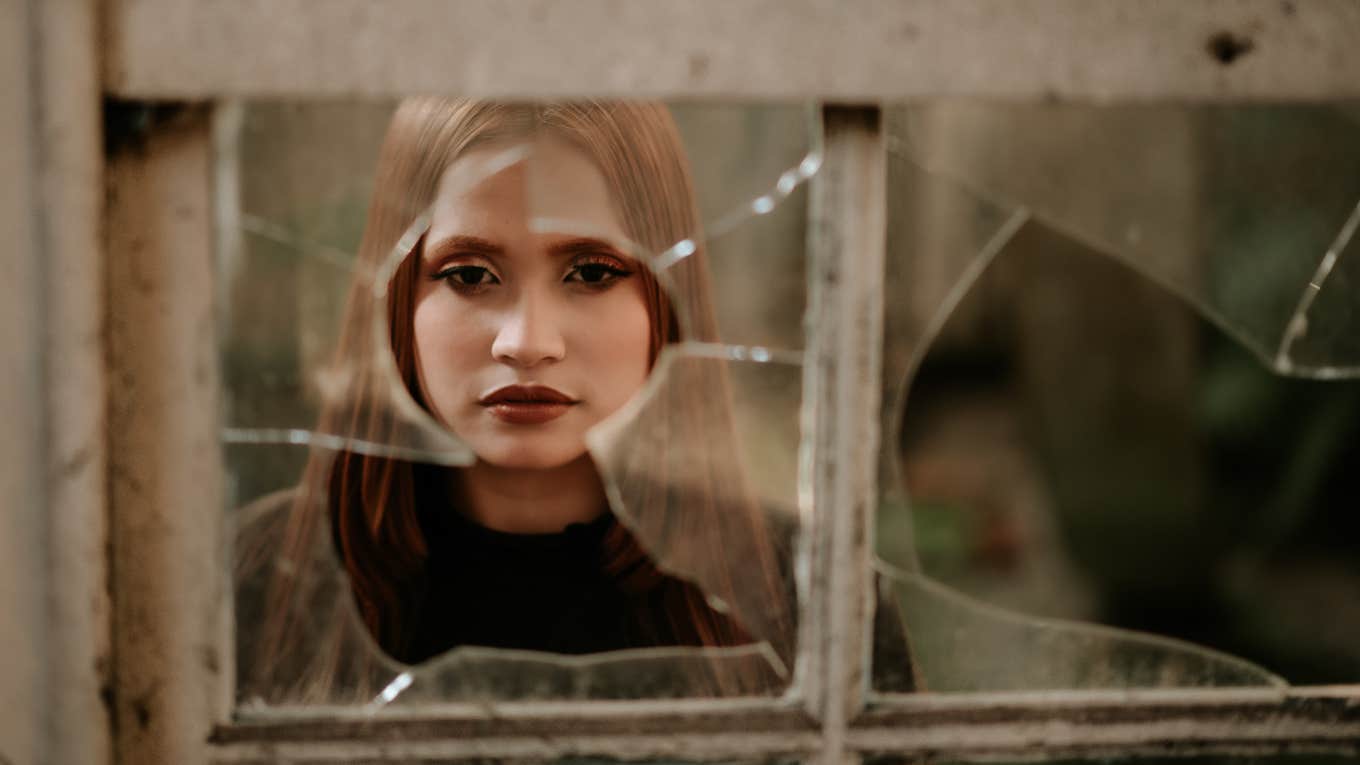 woman looking through broken window