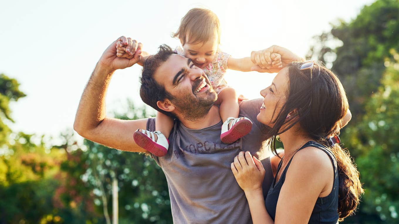 dad with daughter on shoulders and smiling wife outside at park