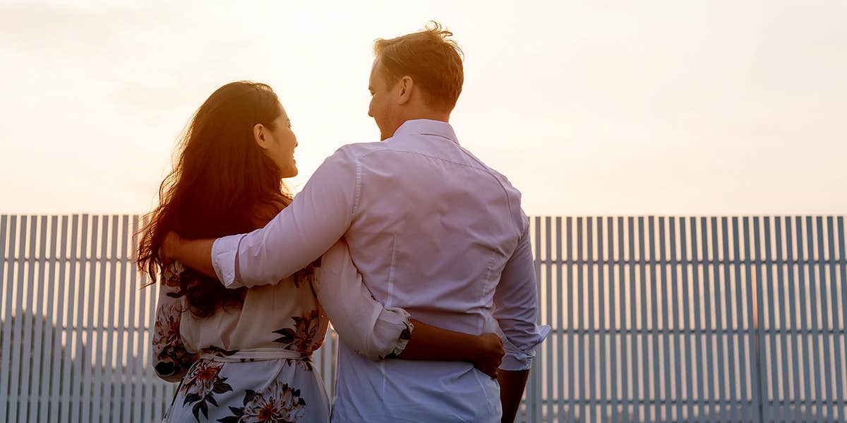 A Man Refused To Marry His Foreign Girlfriend — And She Died As A Result couple with arms around each other watching sunset