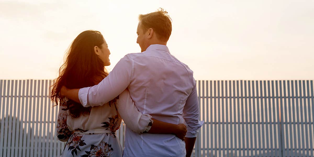 couple with arms around each other watching sunset