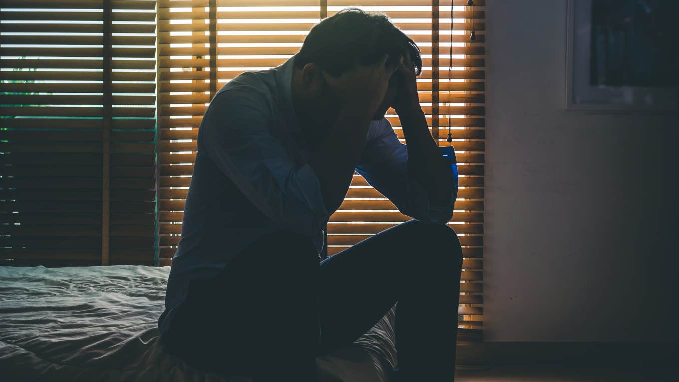 depressed man sitting head in hands on the bed in the dark bedroom with low light environment