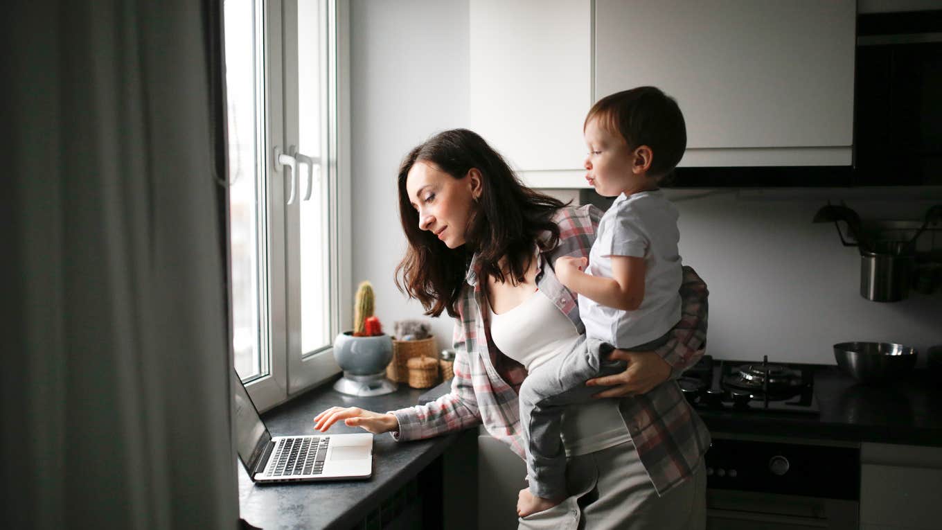 mom with a baby in her arms working on a laptop in the kitchen.