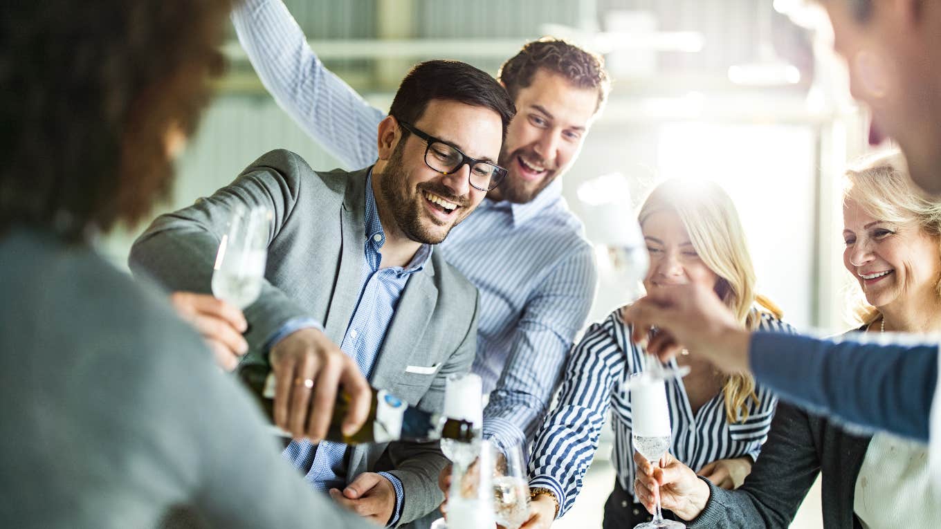 man pouring champagne at a party surrounded by laughing friends