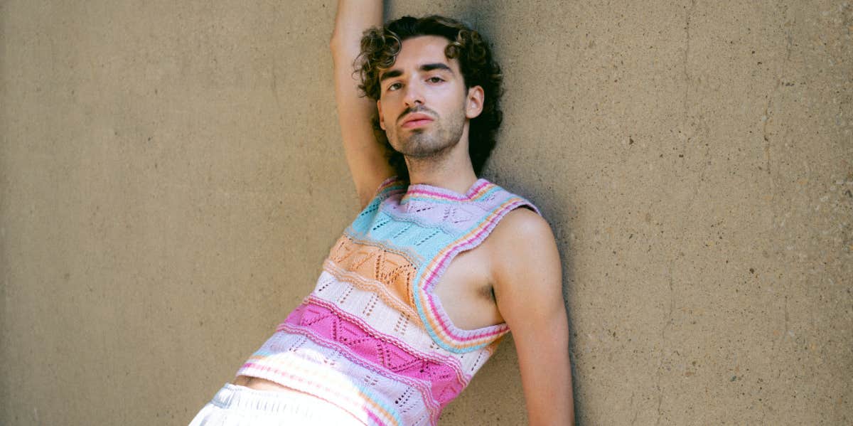 Man wearing a colorful top and posing in front of a wall