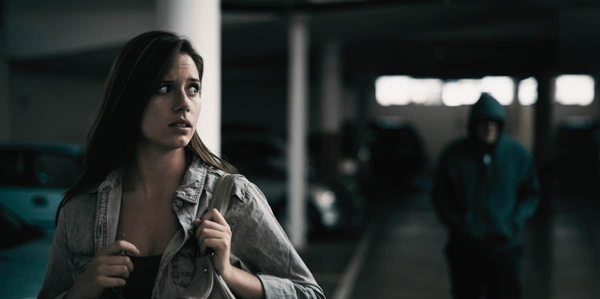 young woman in a parking lot looking concerned as someone follows her.