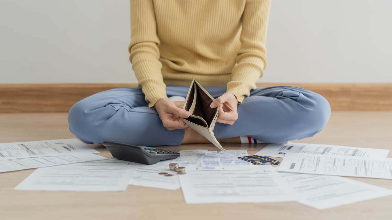 woman sitting on floor with empty wallet surrounded by bills