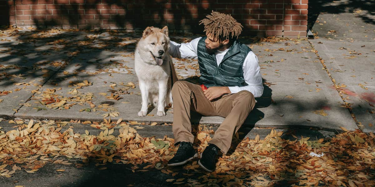 Man with dog sitting on sidewalk