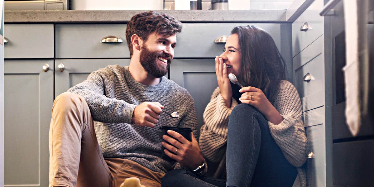 Married couple sitting on kitchen floor smiling at one another