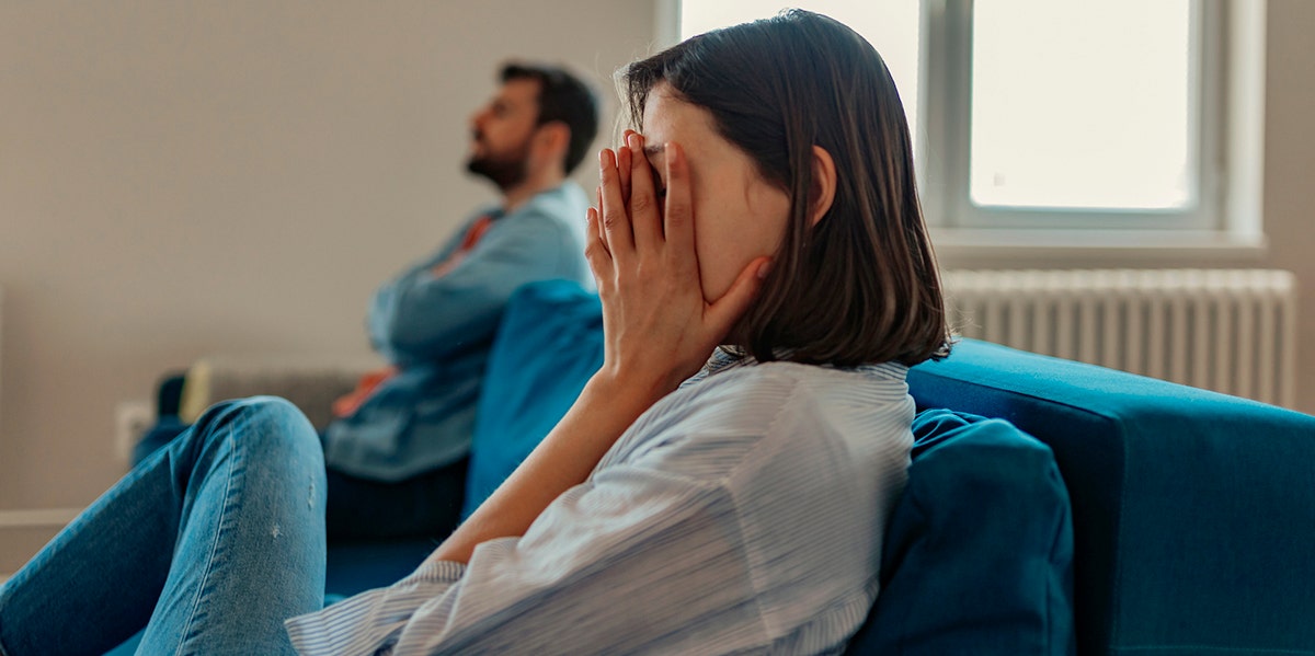 woman putting hand over eyes next to man on couch