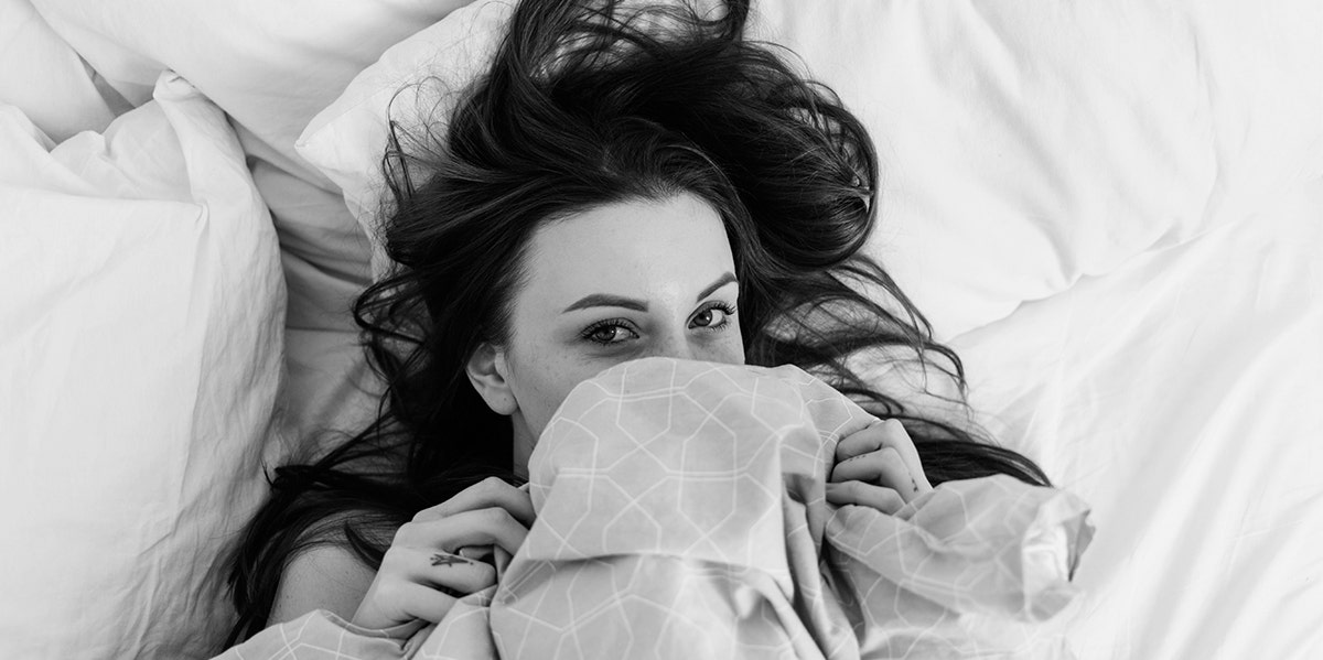 woman covering face under sheets