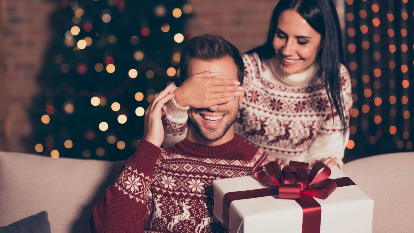 Woman covering boyfriends eyes while holding a holiday gift