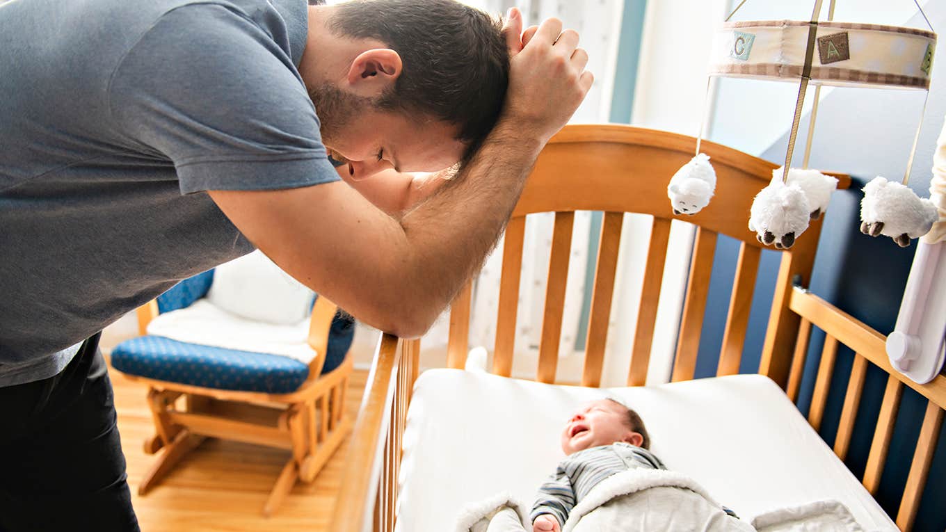 tired father with baby in crib