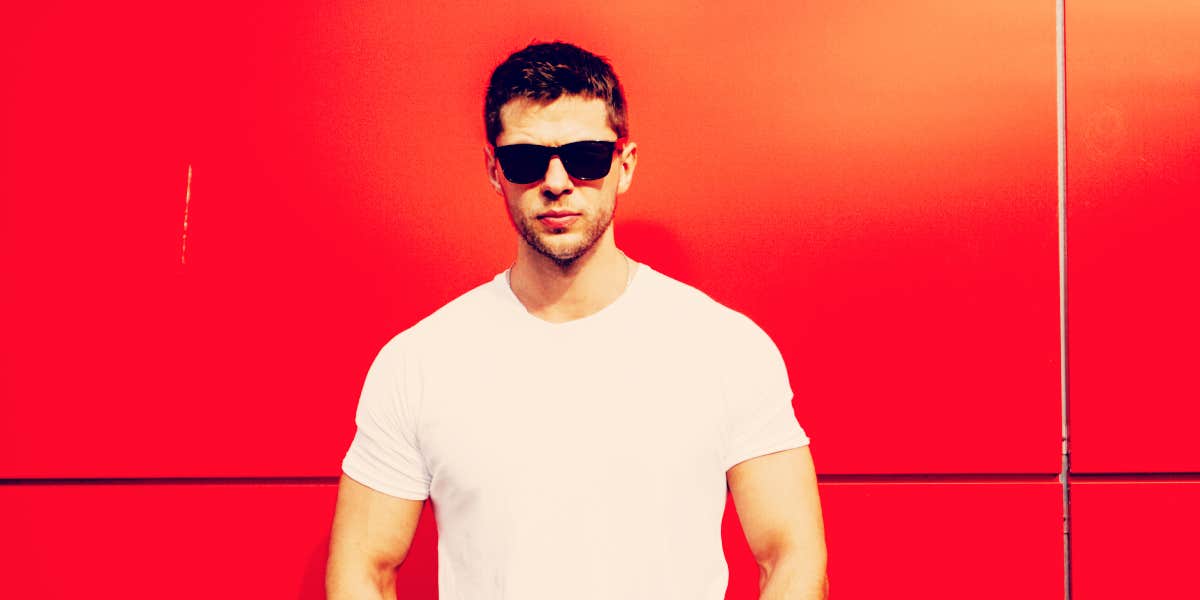 man in sunglasses standing in front of a red-orange wall