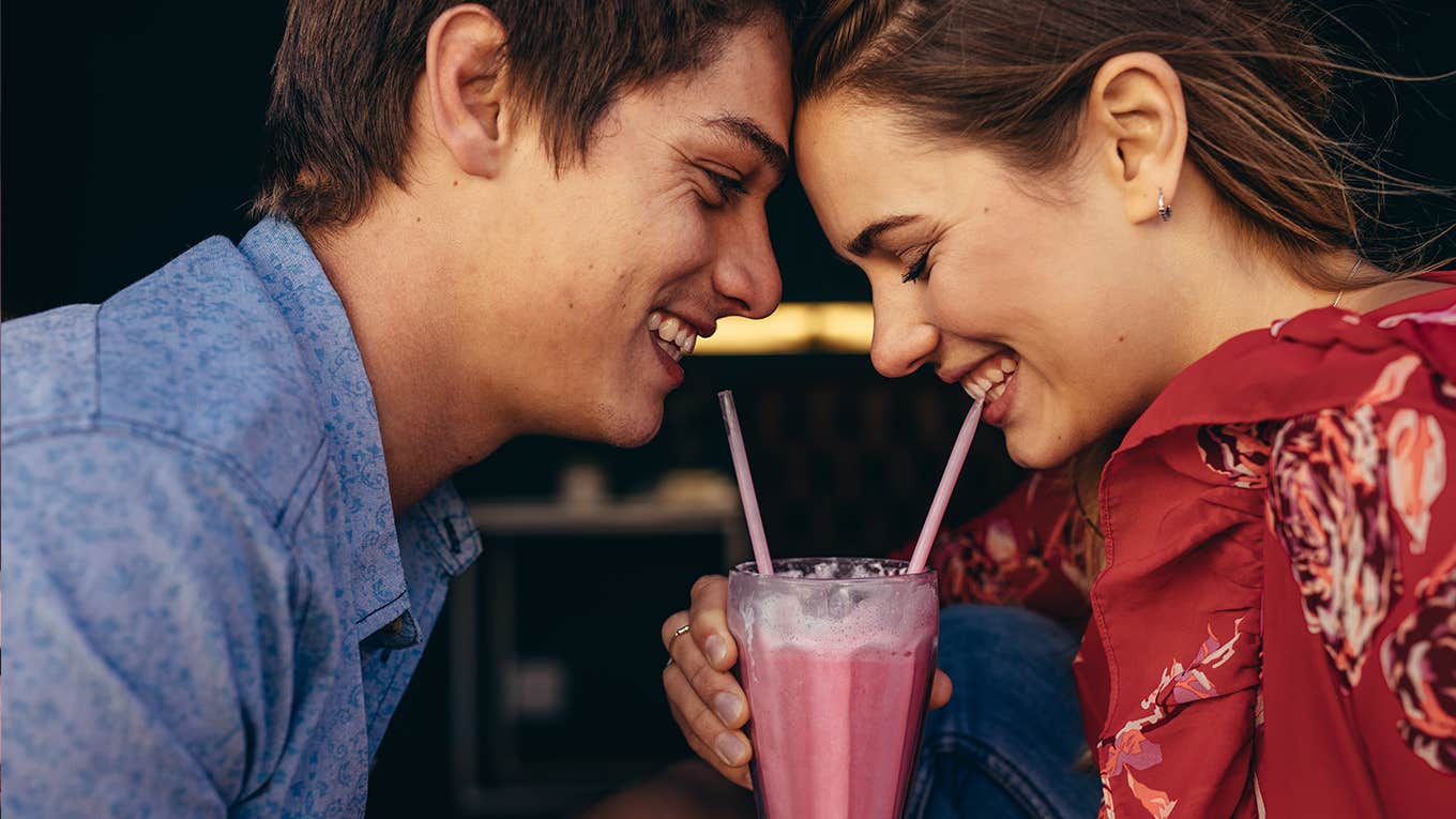 Close up of a happy couple sharing a milkshake with two straws.